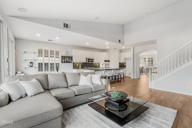 living room with sink, high vaulted ceiling, and light wood-type flooring