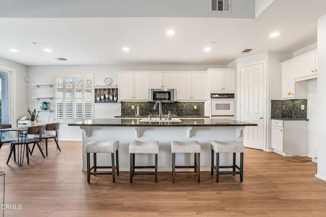 kitchen featuring white cabinetry, sink, dark stone counters, a kitchen island with sink, and light hardwood / wood-style floors