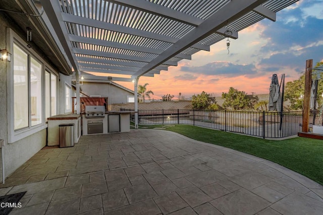 patio terrace at dusk featuring area for grilling, a pergola, a lawn, and an outdoor kitchen