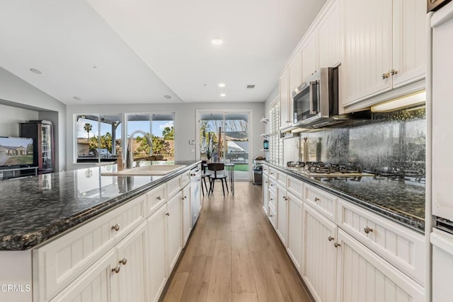 kitchen featuring sink, tasteful backsplash, light wood-type flooring, an island with sink, and stainless steel appliances