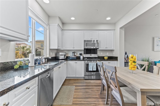 kitchen with dark wood-type flooring, sink, appliances with stainless steel finishes, dark stone counters, and white cabinets