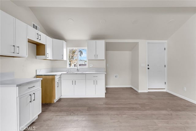 kitchen with sink, light hardwood / wood-style floors, vaulted ceiling, and white cabinets