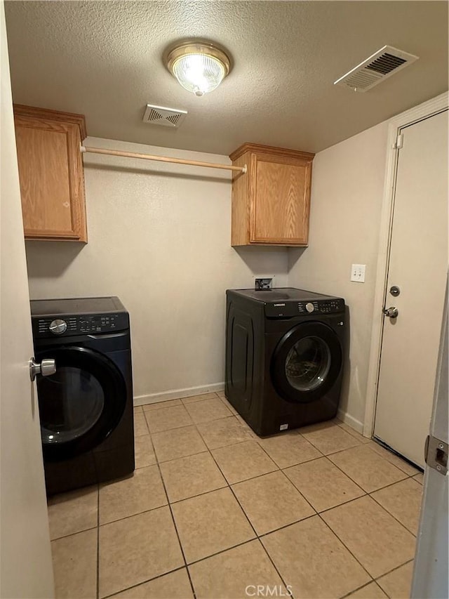 clothes washing area with cabinets, washer / dryer, a textured ceiling, and light tile patterned floors