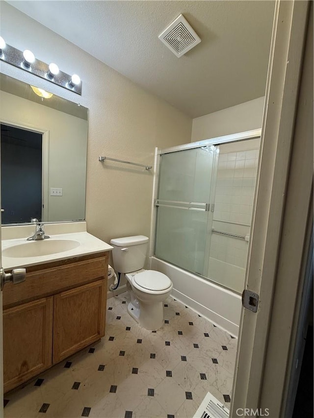 full bathroom featuring vanity, a textured ceiling, enclosed tub / shower combo, and toilet