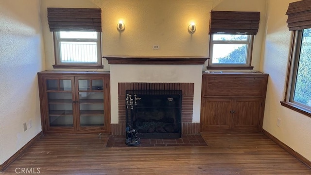 unfurnished living room with a brick fireplace, plenty of natural light, and dark hardwood / wood-style floors