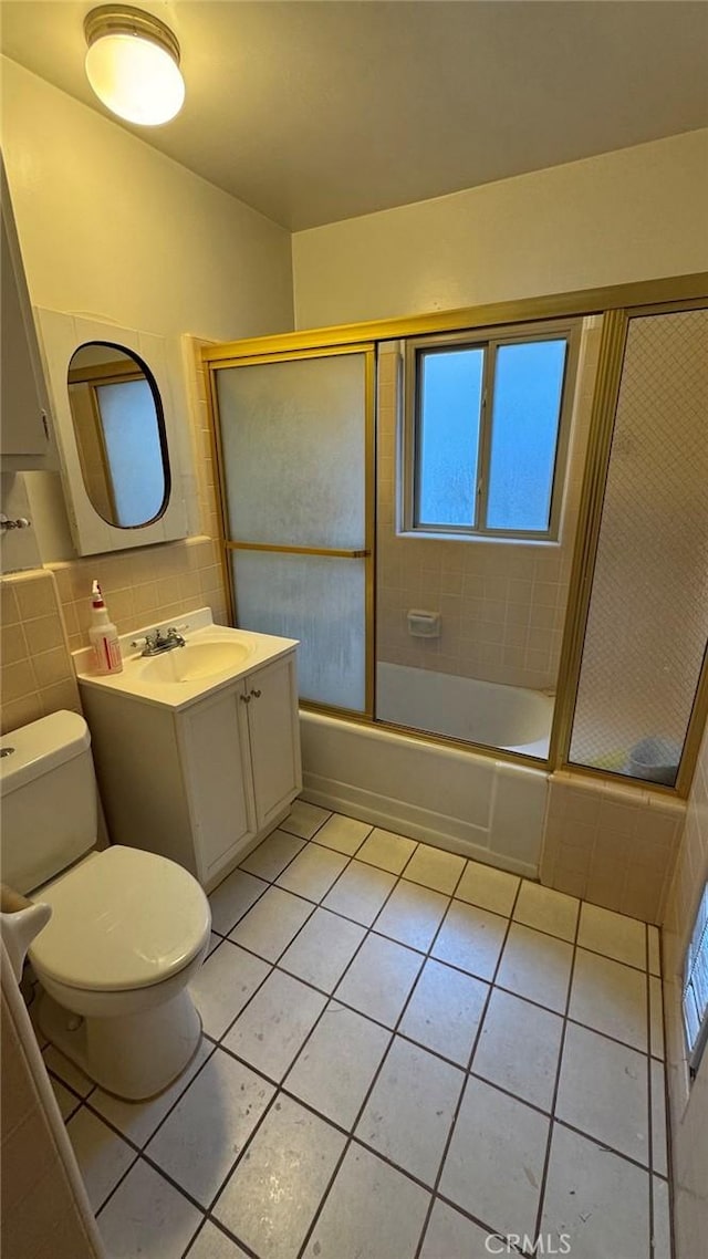 full bathroom with tile patterned floors, toilet, combined bath / shower with glass door, tile walls, and vanity