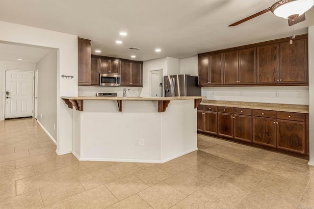 kitchen with a breakfast bar area, light countertops, appliances with stainless steel finishes, ceiling fan, and dark brown cabinets