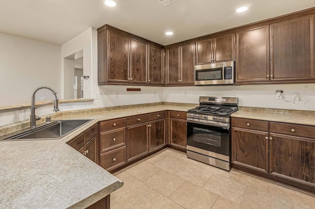 kitchen with appliances with stainless steel finishes, light countertops, a sink, and dark brown cabinetry