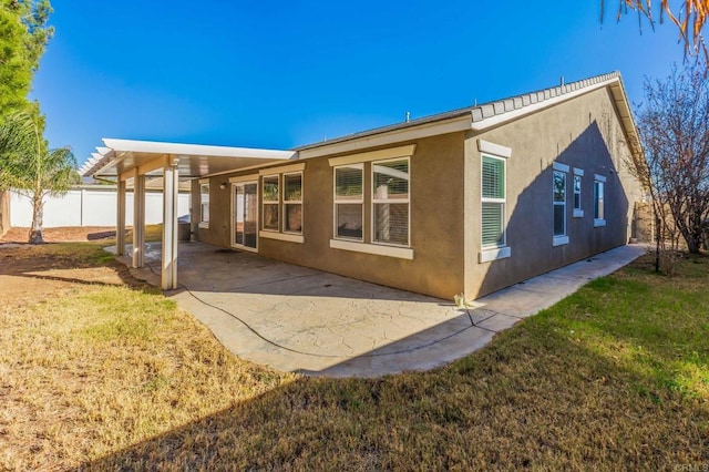 rear view of house with a yard, fence, a patio, and stucco siding