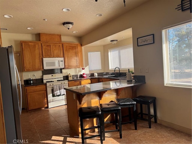 kitchen with sink, a textured ceiling, a kitchen breakfast bar, kitchen peninsula, and white appliances