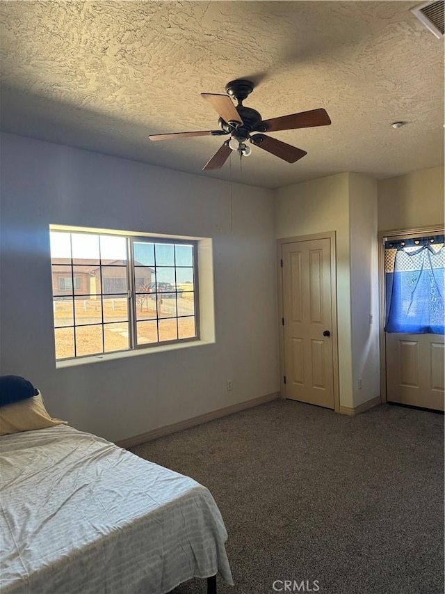 unfurnished bedroom with ceiling fan, dark carpet, and a textured ceiling