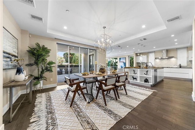 dining space with a raised ceiling, an inviting chandelier, and dark hardwood / wood-style flooring