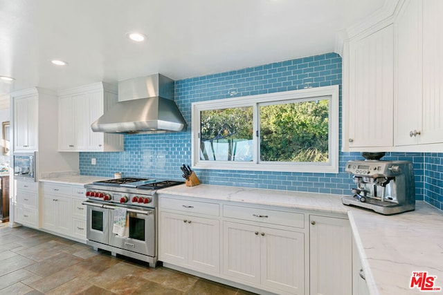 kitchen with white cabinetry, double oven range, light stone counters, decorative backsplash, and wall chimney exhaust hood