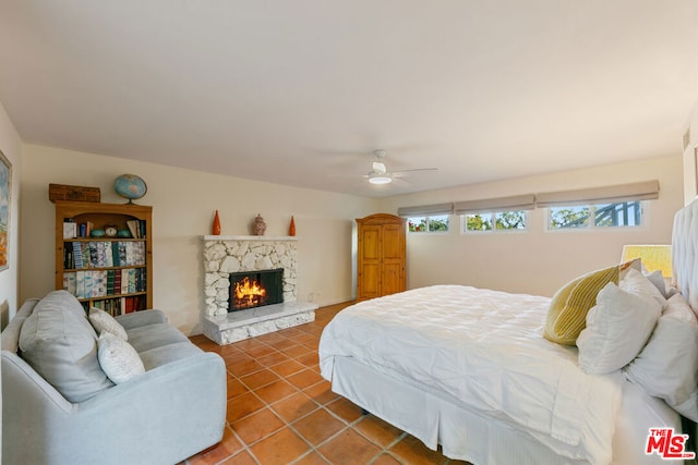 bedroom with a stone fireplace, tile patterned floors, and ceiling fan