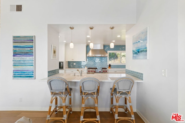 kitchen featuring pendant lighting, a breakfast bar area, kitchen peninsula, and wall chimney exhaust hood