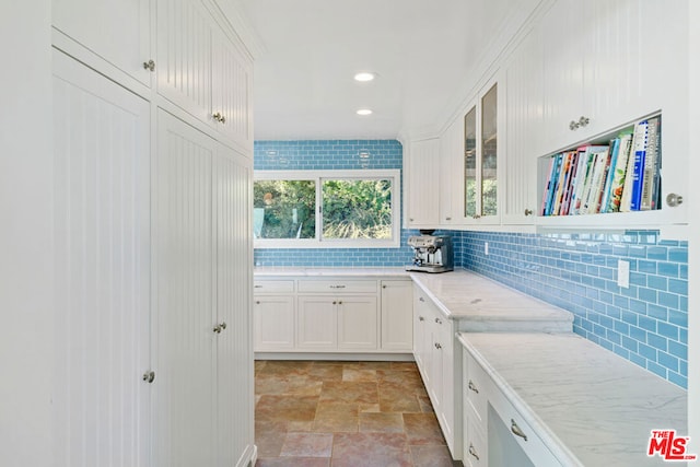 kitchen with light stone counters, white cabinets, and backsplash