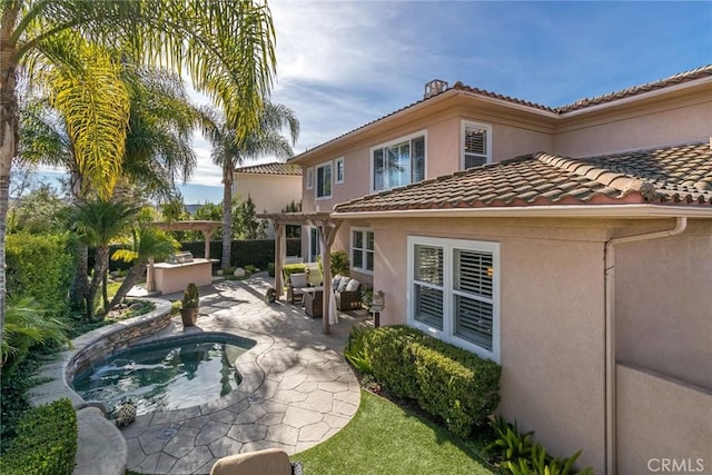 back of house featuring a pergola, a hot tub, exterior kitchen, and a patio