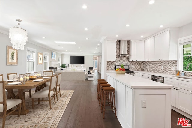 kitchen with sink, white cabinetry, stainless steel appliances, decorative light fixtures, and wall chimney exhaust hood