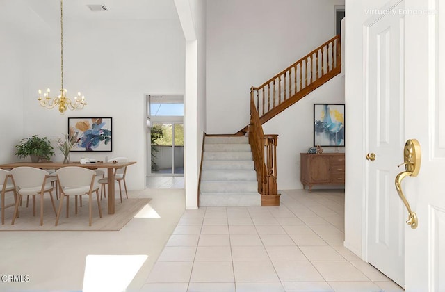 tiled entrance foyer with visible vents, a notable chandelier, a high ceiling, and stairs