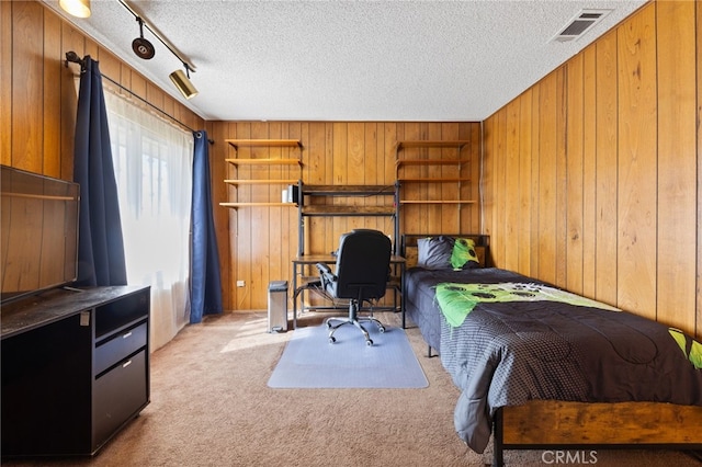 bedroom featuring wooden walls, light colored carpet, track lighting, and a textured ceiling