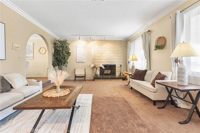living room with a textured ceiling, arched walkways, a brick fireplace, rail lighting, and carpet flooring
