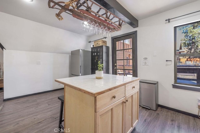 kitchen with a breakfast bar, stainless steel refrigerator, a center island, tile counters, and light brown cabinets