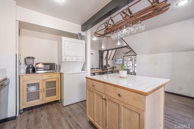 kitchen with tile countertops, dark hardwood / wood-style flooring, stacked washer and clothes dryer, a center island, and stainless steel appliances