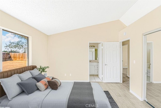 bedroom with vaulted ceiling, a textured ceiling, light hardwood / wood-style floors, and ensuite bath