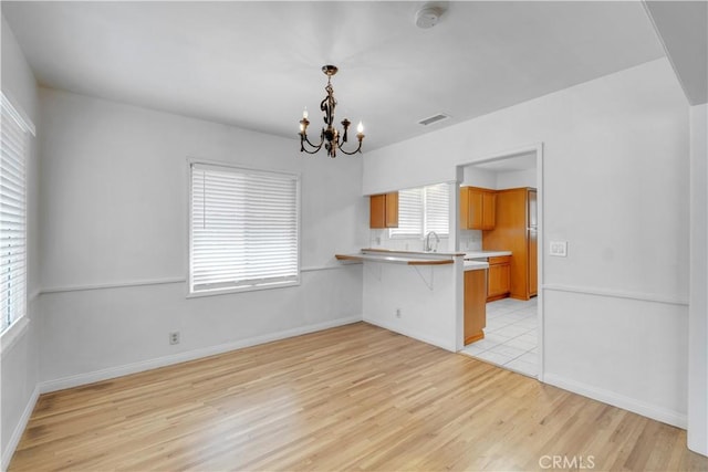 kitchen featuring a kitchen bar, light hardwood / wood-style flooring, kitchen peninsula, a notable chandelier, and pendant lighting