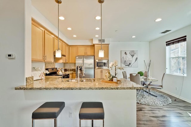 kitchen with appliances with stainless steel finishes, decorative light fixtures, light stone counters, kitchen peninsula, and light brown cabinets