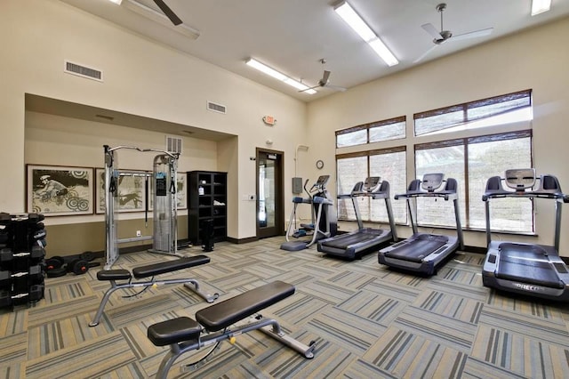 gym featuring a towering ceiling, light carpet, and ceiling fan