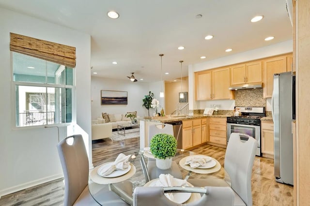 kitchen with light brown cabinetry, decorative light fixtures, kitchen peninsula, stainless steel appliances, and light stone countertops