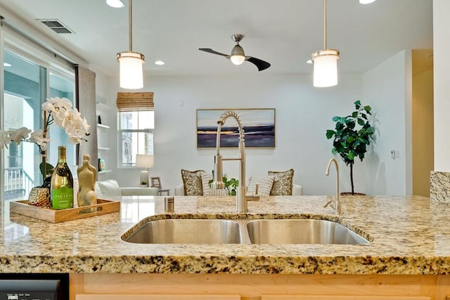 kitchen featuring light stone counters, hanging light fixtures, sink, and ceiling fan