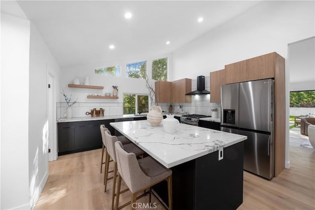 kitchen with wall chimney exhaust hood, a kitchen bar, tasteful backsplash, a center island, and stainless steel appliances