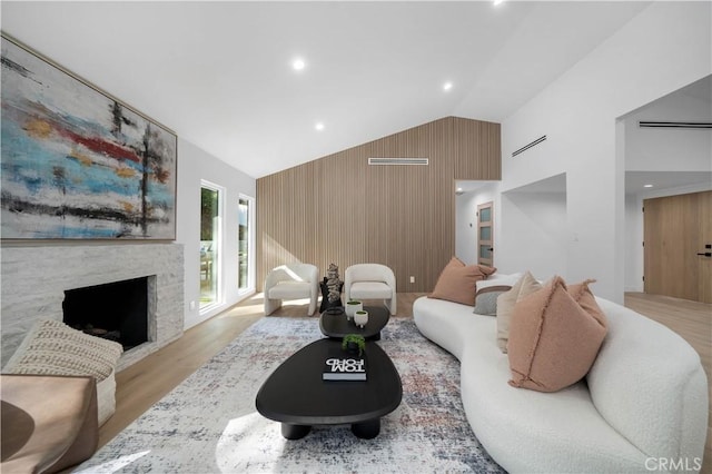 living room with high vaulted ceiling, a fireplace, light hardwood / wood-style floors, and wood walls