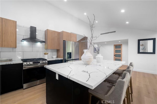 kitchen with stainless steel appliances, a center island, wall chimney range hood, and a kitchen breakfast bar