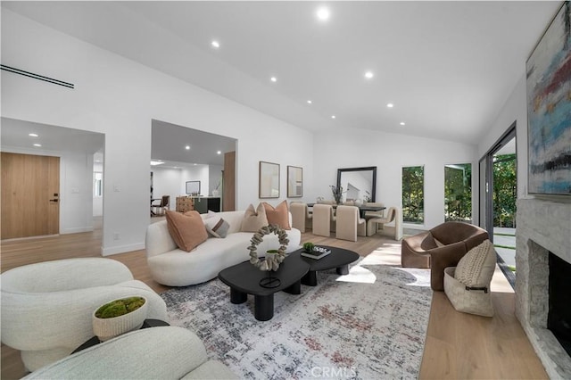 living room featuring high vaulted ceiling, a fireplace, and light hardwood / wood-style flooring