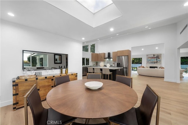 dining room with a high ceiling, light wood-type flooring, and a skylight