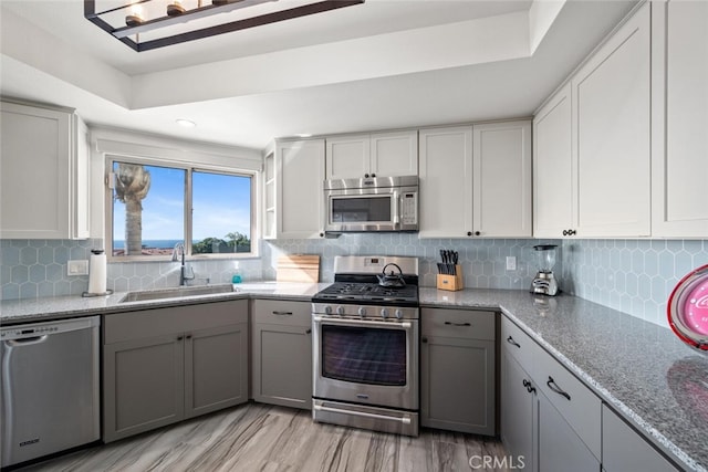 kitchen featuring sink, gray cabinetry, stainless steel appliances, light stone counters, and tasteful backsplash