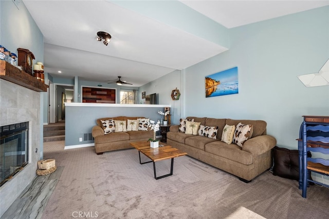 living room featuring a tiled fireplace, carpet, and ceiling fan