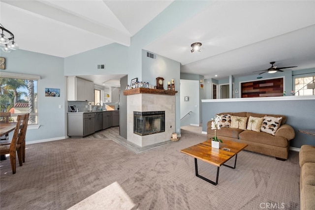 living room with lofted ceiling with beams, a tile fireplace, light carpet, and ceiling fan