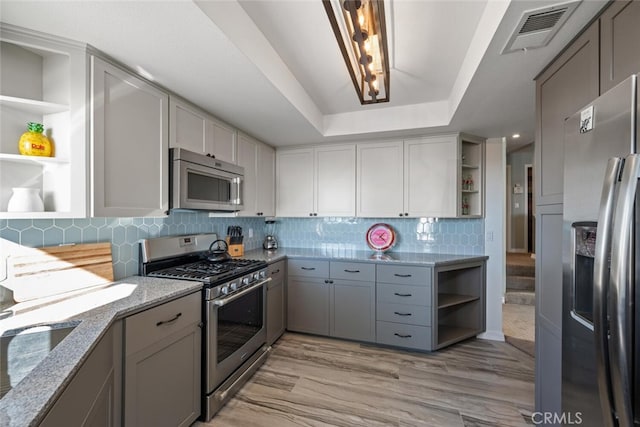 kitchen with stainless steel appliances, a raised ceiling, light stone countertops, and gray cabinets