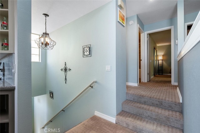 stairway with an inviting chandelier and carpet