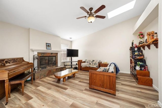 living room with lofted ceiling with skylight, ceiling fan, a fireplace, and light wood-type flooring