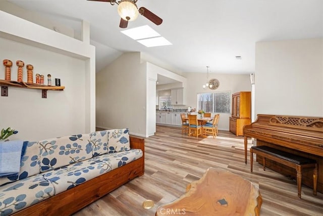 living room with ceiling fan, lofted ceiling with skylight, and light hardwood / wood-style flooring