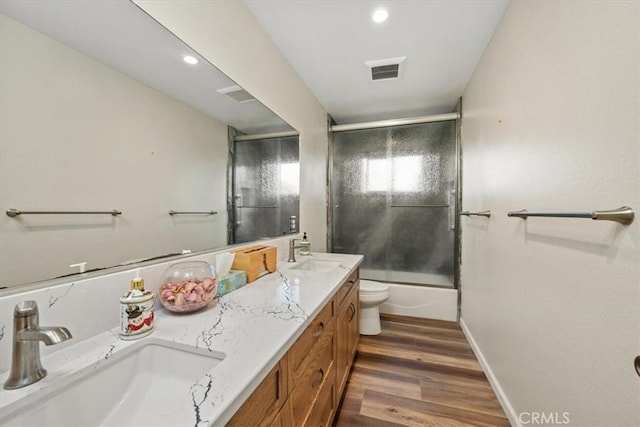 full bathroom with hardwood / wood-style flooring, enclosed tub / shower combo, vanity, and toilet