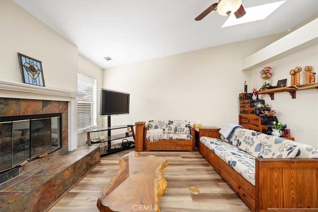 living room with ceiling fan, a tile fireplace, and light wood-type flooring