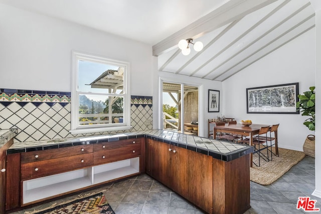 kitchen with tasteful backsplash, vaulted ceiling with beams, tile counters, kitchen peninsula, and an inviting chandelier