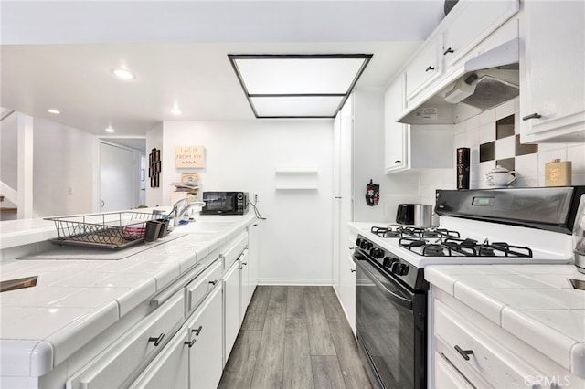 kitchen featuring backsplash, tile countertops, range with gas stovetop, and white cabinets