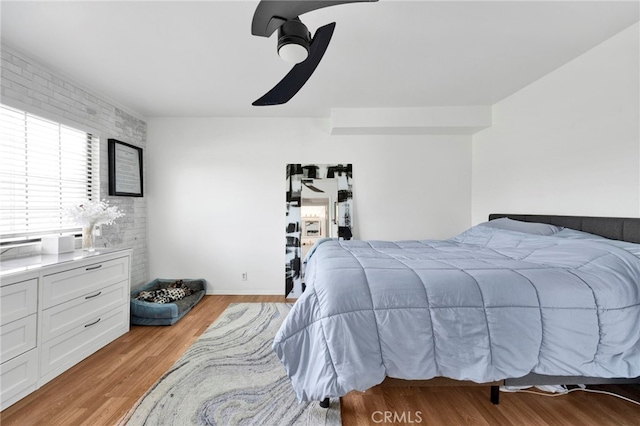 bedroom featuring ceiling fan, brick wall, and light hardwood / wood-style floors